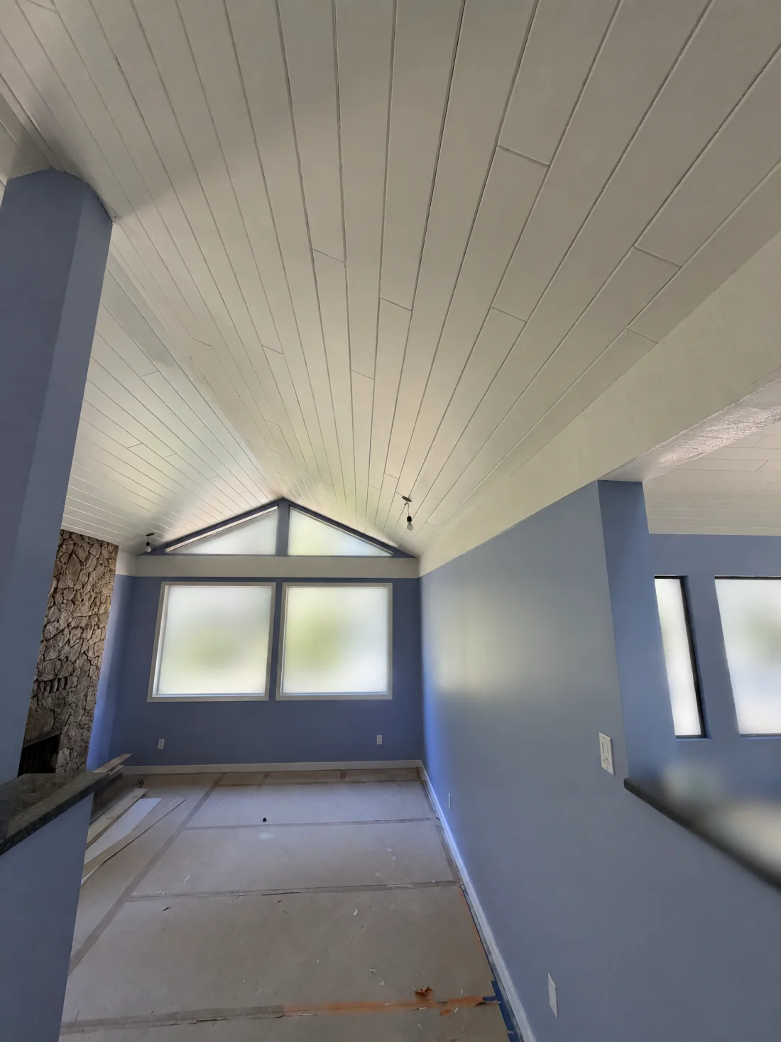 Vaulted plank ceiling and adjoining blue interior walls during paint matching work, with window views privacy-blurred.