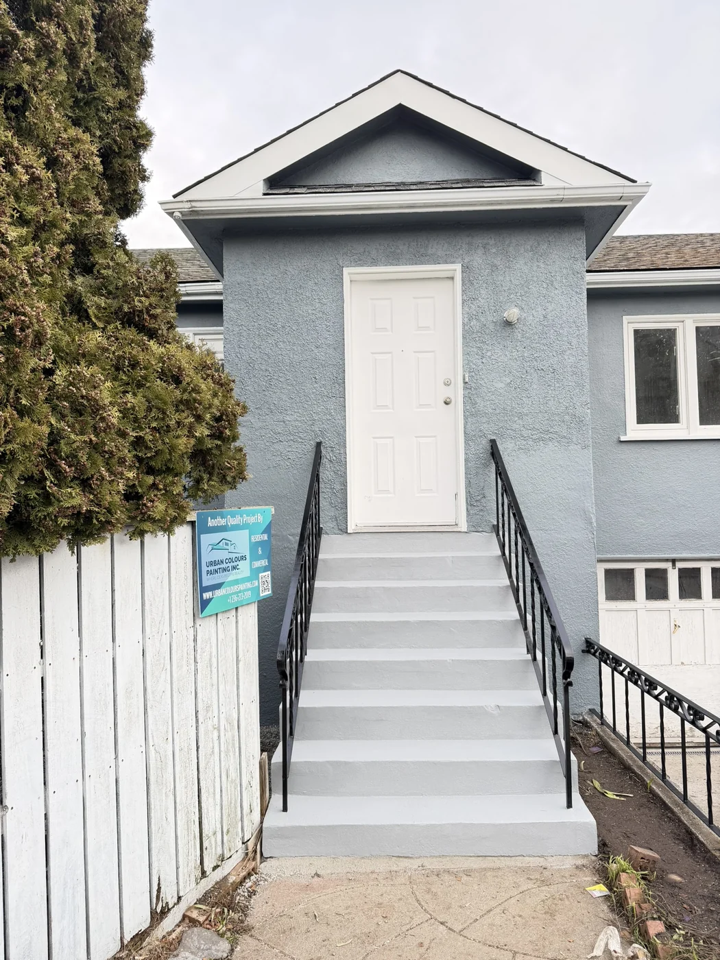Completed exterior painting on a residential home with blue-grey walls and white trim