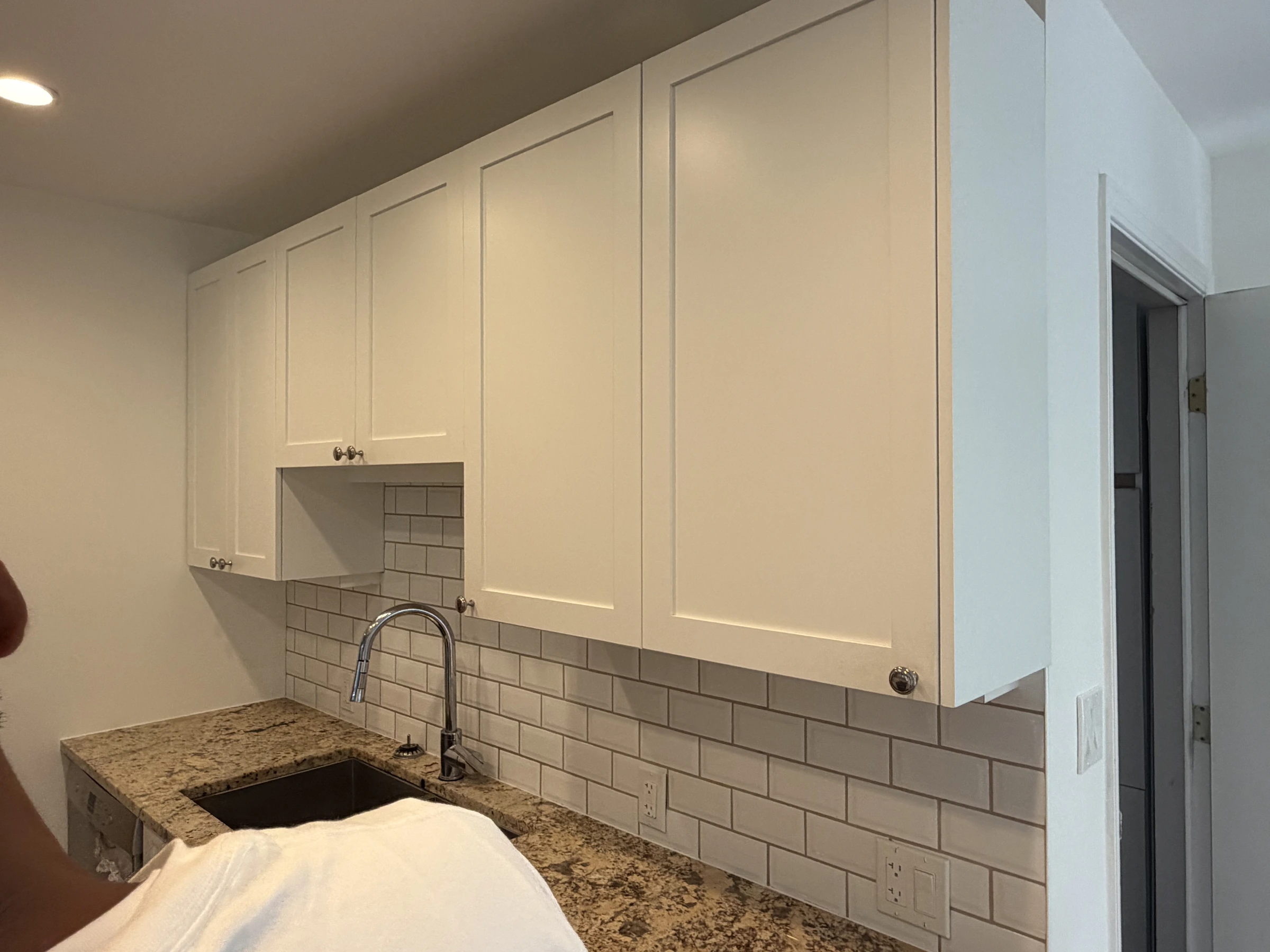 Before photo of white upper kitchen cabinets above a tiled backsplash