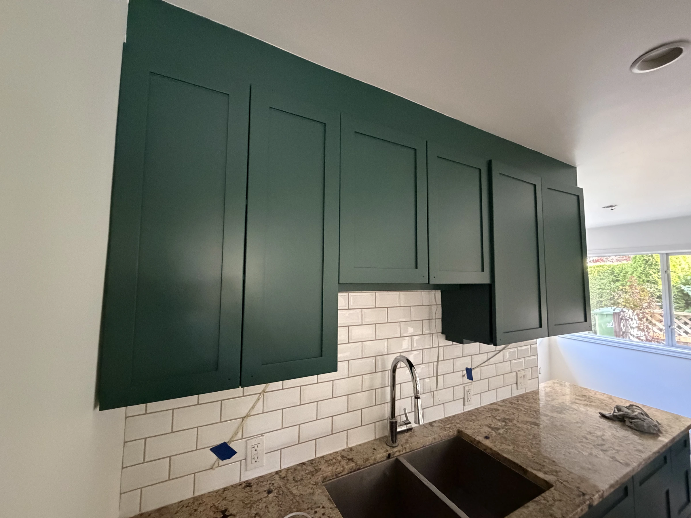 Close view of deep green upper and lower kitchen cabinets with tiled backsplash
